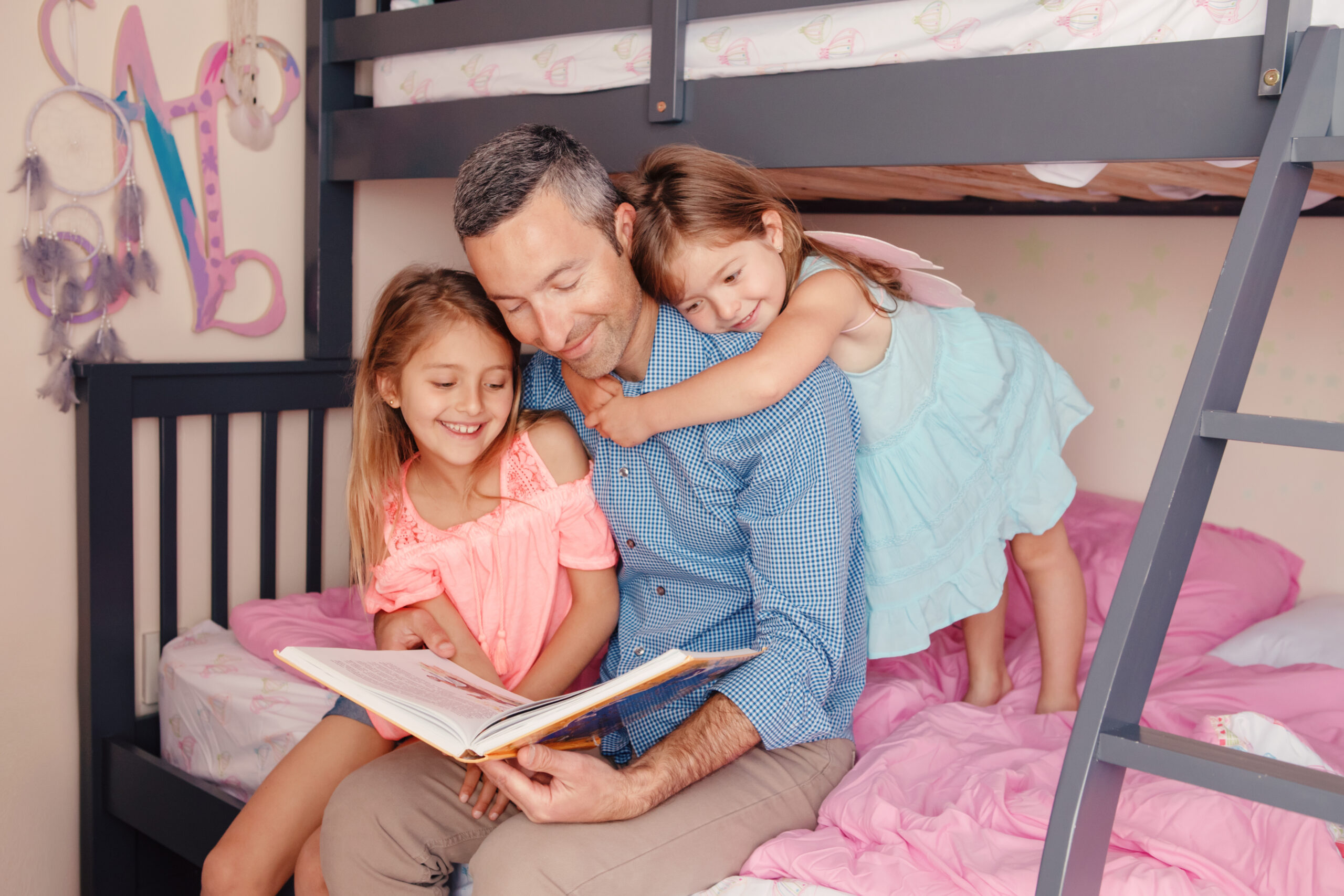 Dad reading book to daughters girls. Family of three people sitting on bed in bedroom. Happy father and children at home spending time together. Education and happy lifestyle childhood.