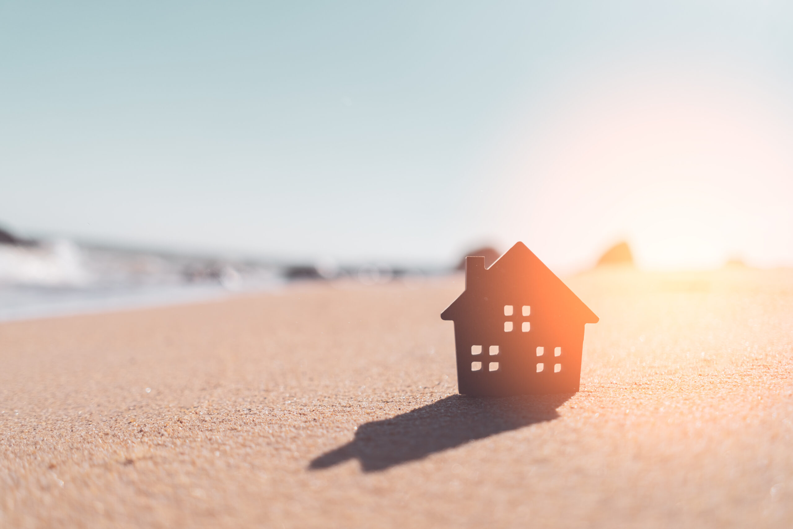 Small home model on sunset beach sand texture background.